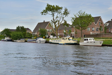 Fototapeta na wymiar Kanał żeglowny z łódkami przy brzegu wśród drzew i domów mieszkalnych.