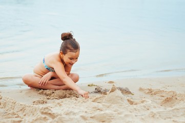 Fototapeta na wymiar Adorable little girl building a sandcastlle at the seashore