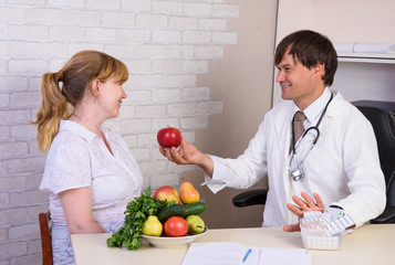 Smiling doctor holds out fruit to a pregnant young woman.