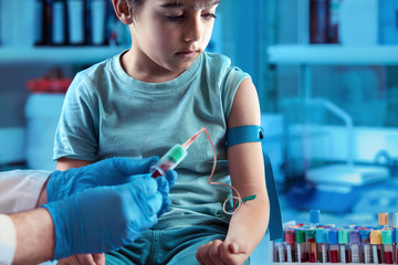 technician making blood tests on a young boy in the laboratory of blood extractions / Doctor taking...