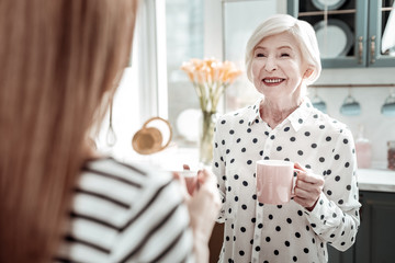 Cheerful senior woman smiling while standing with tea and talking