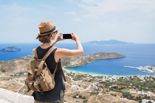 Young tourist woman using smartphone taking photo of beautiful landscape with sea in Greece. Traveler girl with backpack and mobile phone. Travel, tourism, summer holidays, active lifestyle concept