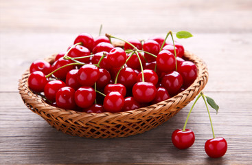 Cherry in wooden basket with leaves on grey table.