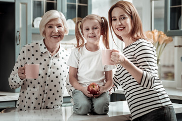 Pretty girl sitting between her mother and grandmother with apple in her hand