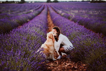 .Beautiful young woman relaxed and carefree enjoying a summer sunset with her lovely dog, a golden retriever, in a colorful lavender field. Lifestyle.