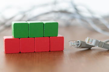 Green and red wooden cubes beside grey lan cable on wooden table 