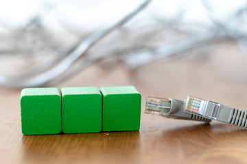 Three green wooden blocks with copyspace on the front beside grey lan cable on wooden table 