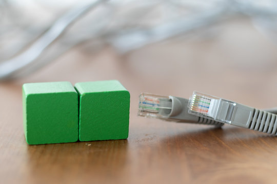 Two green wooden blocks with copyspace on the front beside grey lan cable on wooden table 