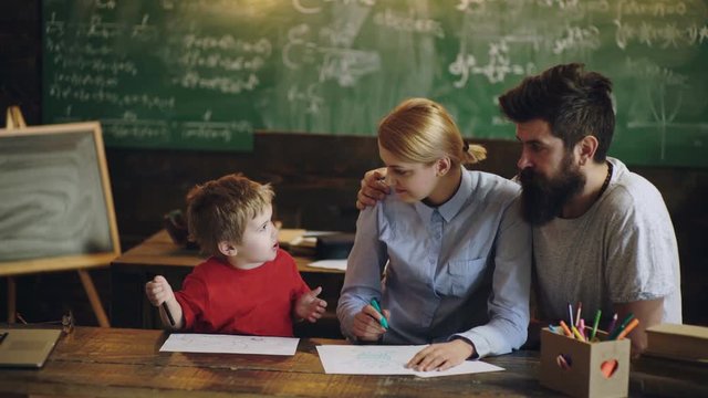 Happy family young parents drawing coloring picture with pencils helping cute child boy enjoying talk play. Background of a green school board. Process of learning at school. Educational process.