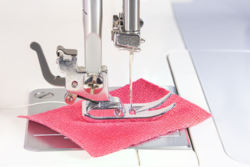 The needle of the sewing machine sews red cloth. The foot of the machine is covered with dust and fibers