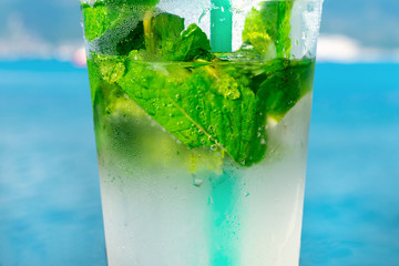 Summer cooling drink. Mojito cocktail on the blue sea background. Refreshments. Closeup.