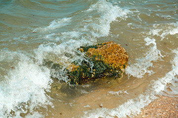 Splashing wave crashing against stones on the seashore with spray.