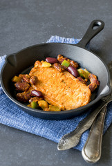 A cooked steak with vegetables in a cast iron frying pan on a dark stone background