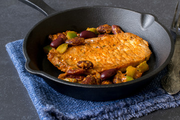 A cooked steak with vegetables in a cast iron frying pan on a dark stone background