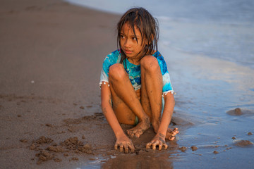 young beautiful and happy Asian American mixed ethnicity child girl 7 or 8 years old playing with sand having fun enjoying Summer holidays isolated on sea background