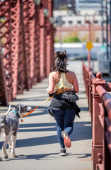 Girl in sportswear runs with dog on leash over truss bridge