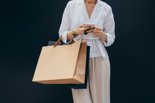 Unrecognisable cropped woman holding shopping bags and typing on her smartphone.