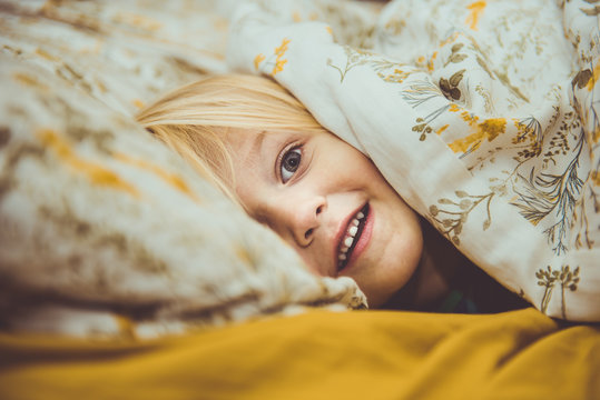 focused photo of girl hiding on a floral bed comforter