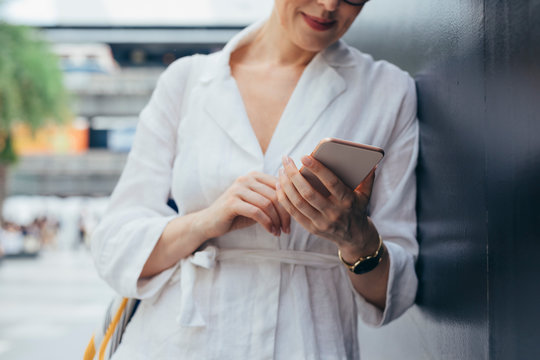 Hands of unrecognisable cropped casual woman stading outdoors and typing on her cell phone.