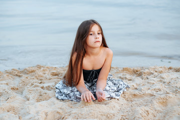 Little girl with long hair in summer dress playing with sand on the beach