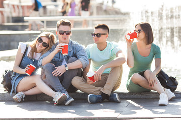 Fototapeta premium Group of young people near the fountain drinking coffee and having fun. friends relaxing outdoors.