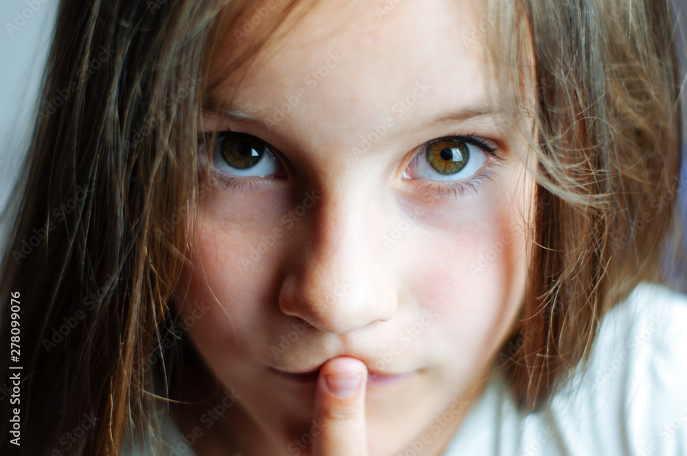 Wall mural Beautiful young girl with long hair puts a finger in her mouth, close portrait