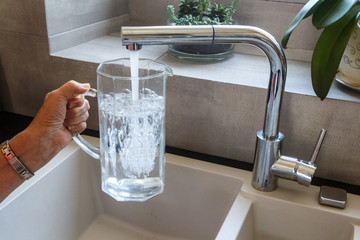 To fill a glass jug with tap water at the sink in a kitchen - 278099008