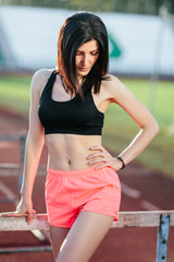 Portrait of Young brunette woman athlete on stadium sporty lifestyle standing on track posing near the barriers running jumping to camera smiling playful