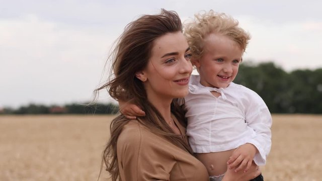Young cute mother with curly child boy son hugging and spinning together walking in wheat field countryside nature