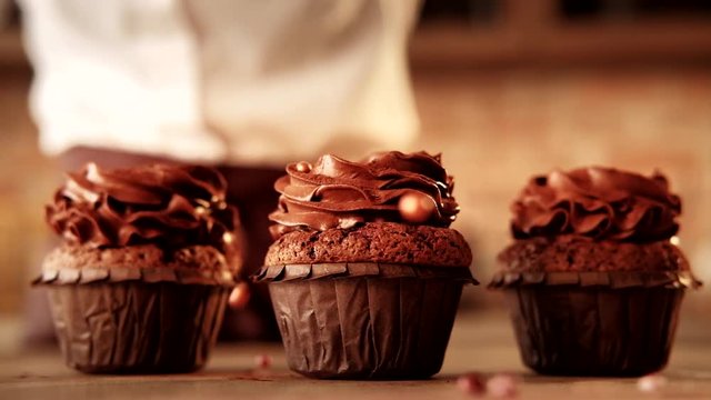 Pastry courses. Chocolate cupcakes with frosting. Sugar beads falling looped