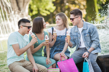 Group of young cheerful people eating ice cream and having fun. Shoppers outdoors. People after shopping. Funny group of friends resting near the fountain.