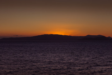 Sun setting behind the profile of island carpeted with wind turbines