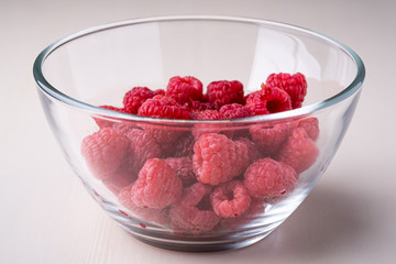 Raspberry red berries in transparent glass bowl plate tasty sweet bright on white background copy space macro