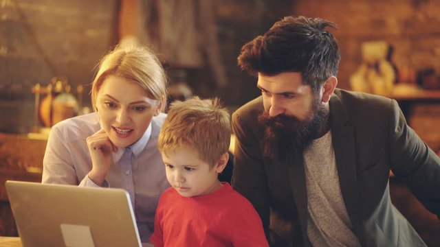 Cute little child boy looking at laptop screen watching cartoons with parents at home. Happy mom dad and small kid boy using computer together enjoying do internet shopping talking.