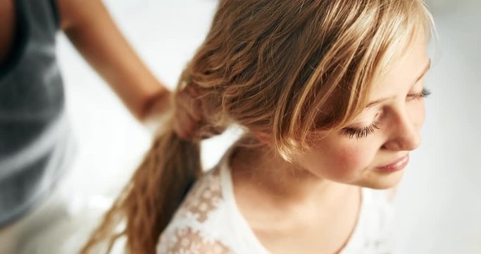 Mother's hands combing long blond daughters hair, attractive girl sitting, face closeup