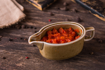 Tomato hot chili sauce with greens in a sauce-pan on rustic wood background