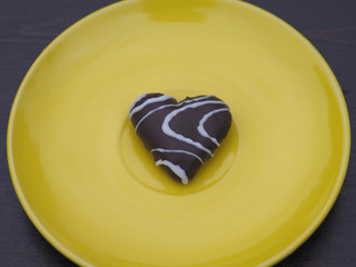 Fototapeta premium A beautiful chocolate heart with white glaze is on a yellow background in the center. Romantic and spectacular picture for design.