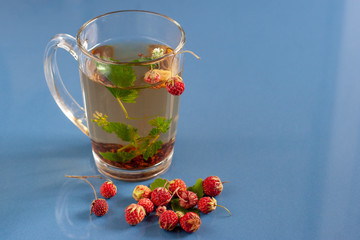 Still life of a mug of herbal tea on blue ceramic tiles with dust texture and reflection. Near scattered strawberries. With space for text. Selective focus.