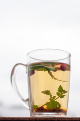 Still life cup with herbal tea. White sky on the background. Strawberry leaves and berries are floating in the cup. Side view. Vertical frame.