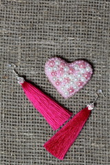 Earrings, tassels lie on a rough linen fabric. Near the decoration in the form of a heart. View from above.