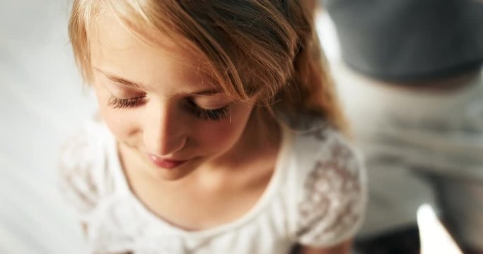 Cute teenage girl sitting with eyes closed while female hands combing her long blond hair
