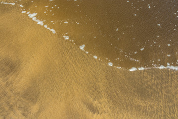 Wet natural sand beach and smooth wave surf texture background. Summer vacation and business travel freedom adventure concept. Close up selective focus