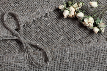 Coarse linen fabric. On it are dried beige roses and a bow of linen threads.