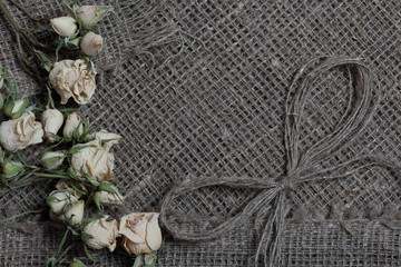 Coarse linen fabric. On it are dried beige roses and a bow of linen threads.