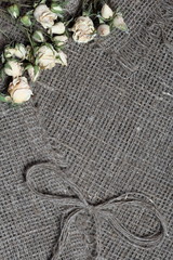 Coarse linen fabric. On it are dried beige roses and a bow of linen threads.