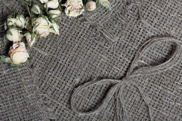 Coarse linen fabric. On it are dried beige roses and a bow of linen threads.