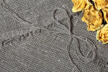 Coarse linen fabric. On it are dried yellow roses and a bow of linen threads.