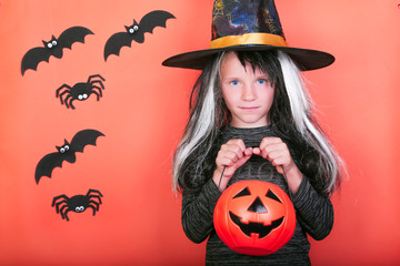laughing child girl with pumpkins in witch costume on Halloween party. Halloween celebration concept, orange scary background with spiders and bats