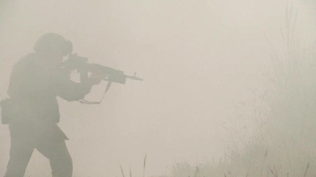 A military soldier with a gun in his hands and a helmet moves cautiously through the fog and thickets