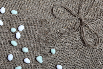 Bright pebbles lie on a rough linen fabric. Near a bow of linen thread.